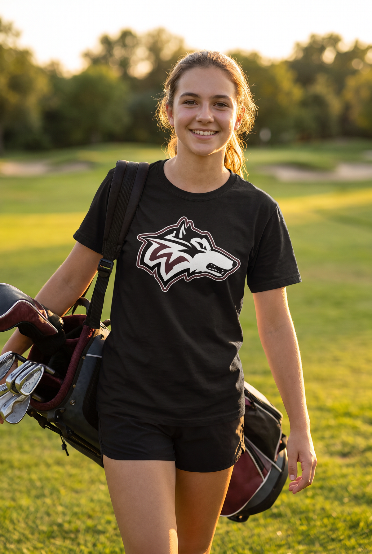 Woodcreek Girls Golf Value Tee in Black, second view carrying a bag up the fairway