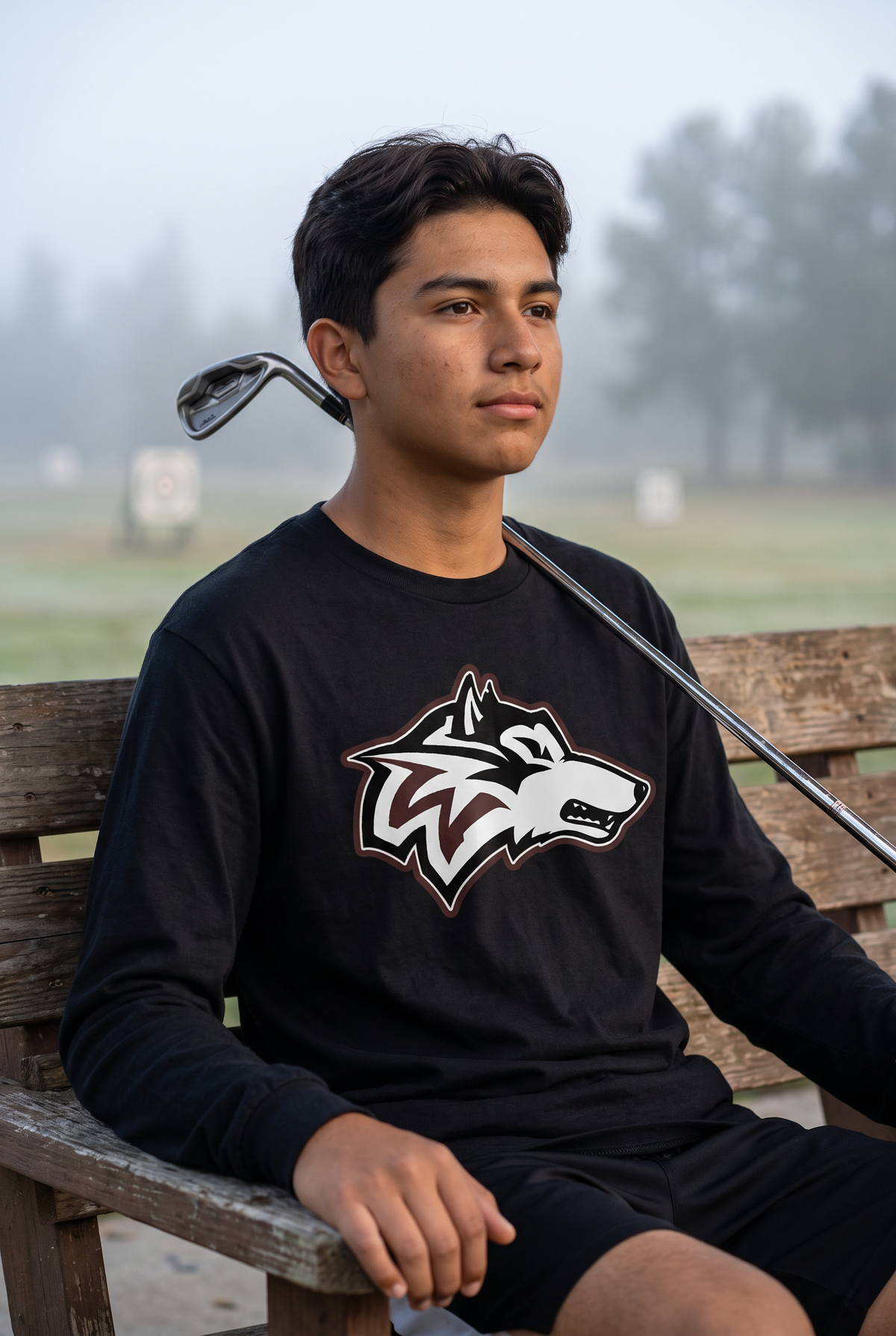 Woodcreek Boys Golf Long Sleeve Tee in Black with the Woodcreek wolf head across the chest, worn at the driving range