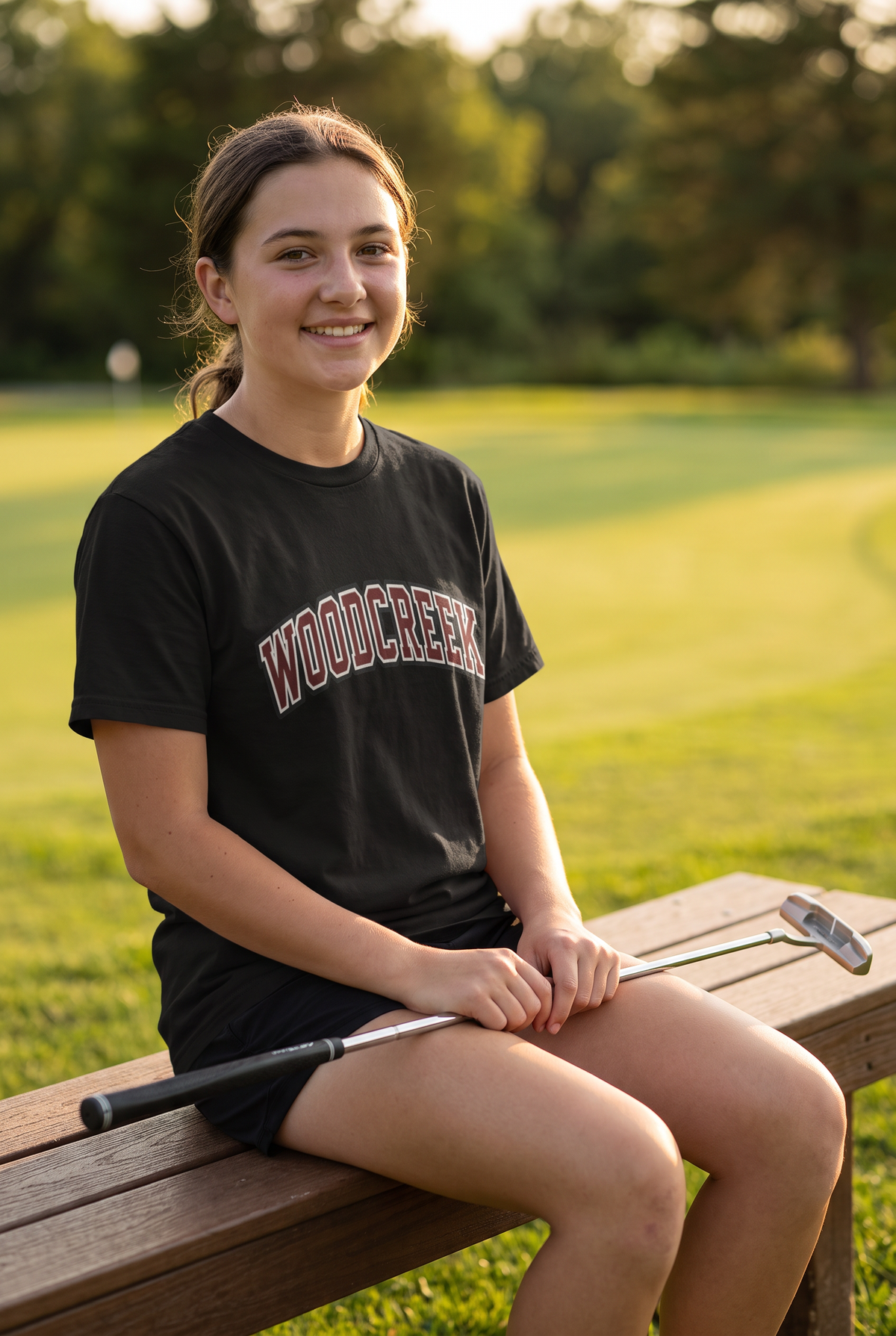 Woodcreek Girls Golf College Letter Value Tee in Black with arched Woodcreek lettering, worn by the putting green