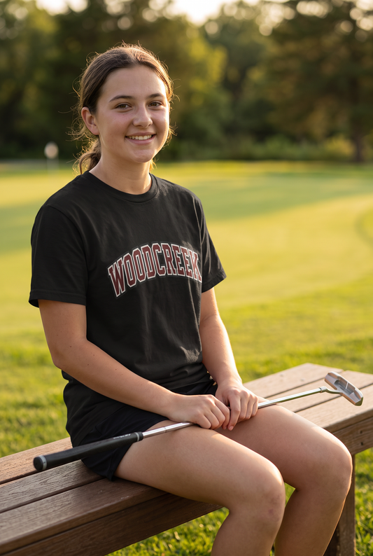 Woodcreek Girls Golf College Letter Value Tee in Black with arched Woodcreek lettering, worn by the putting green