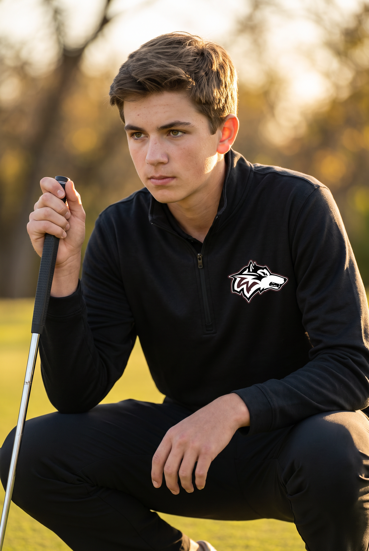 Woodcreek Boys Golf Quarter Zip in Black with the Woodcreek wolf head on the left chest, worn reading a putt at golden hour