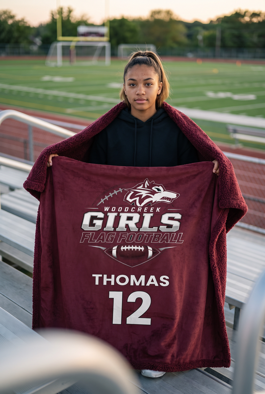 Woodcreek Girls Flag Football personalized sherpa blanket, held open on the bleachers at golden hour