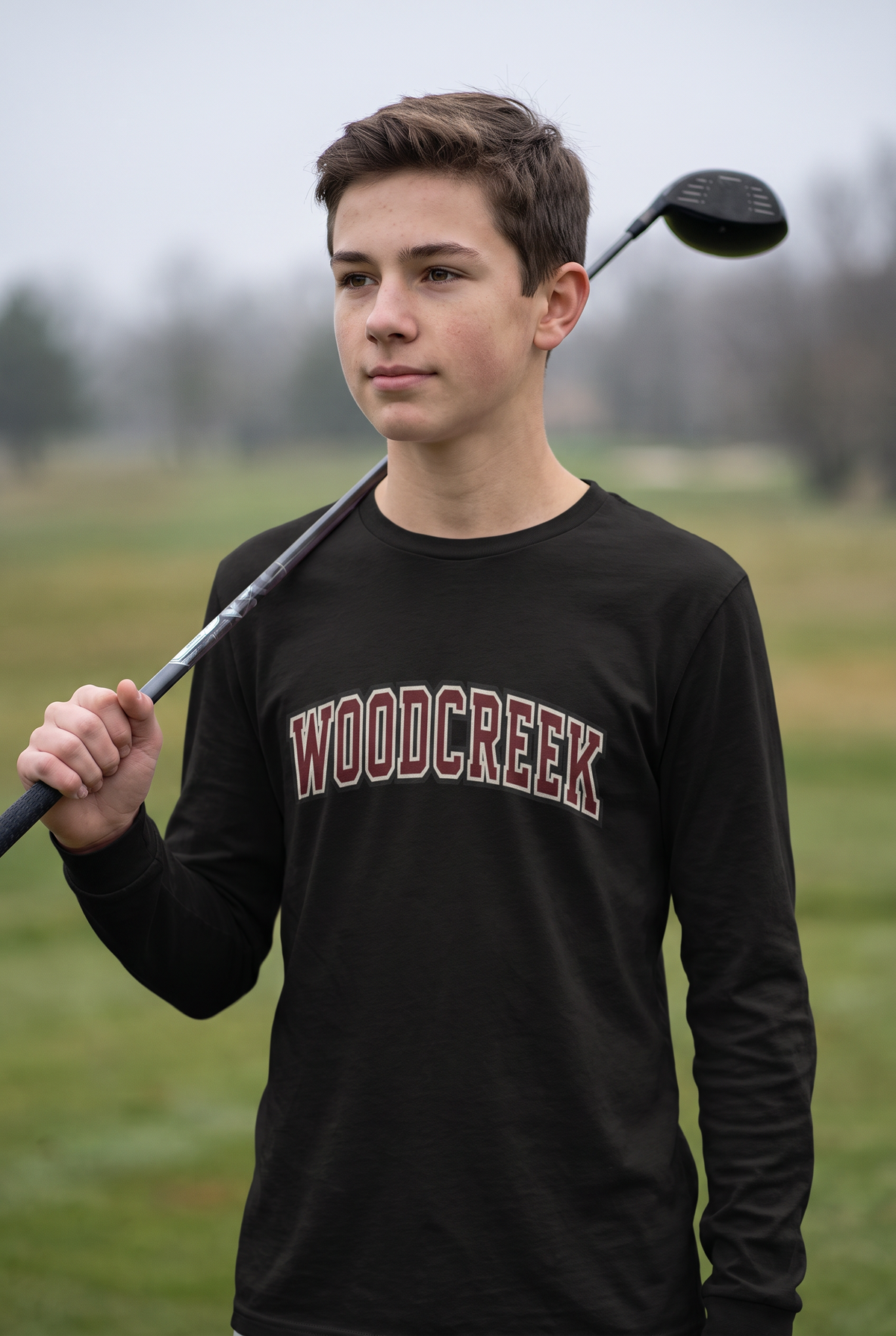 Woodcreek Boys Golf College Letter Long Sleeve Tee in Black with arched Woodcreek lettering, worn on the fairway