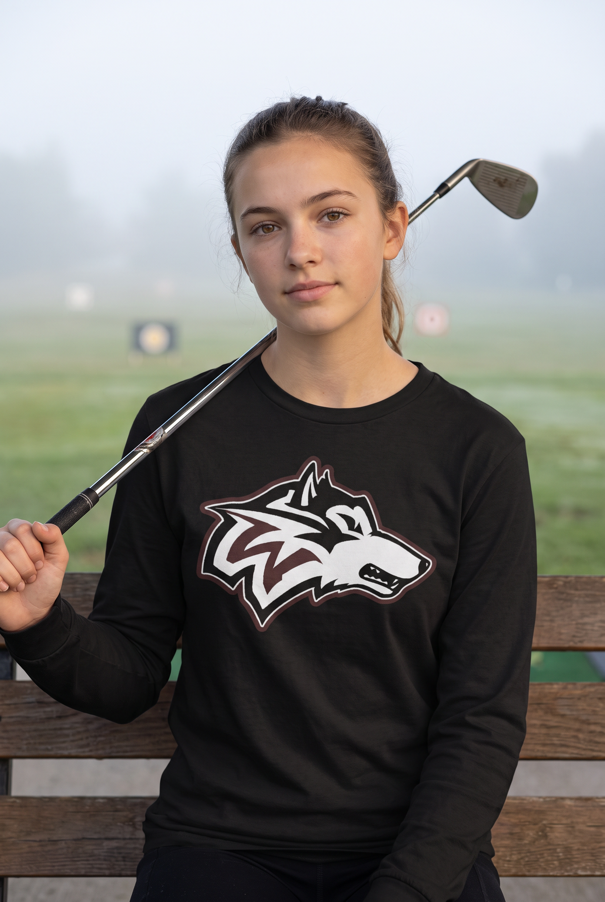 Woodcreek Girls Golf Long Sleeve Tee in Black with the Woodcreek wolf head across the chest, worn at the driving range