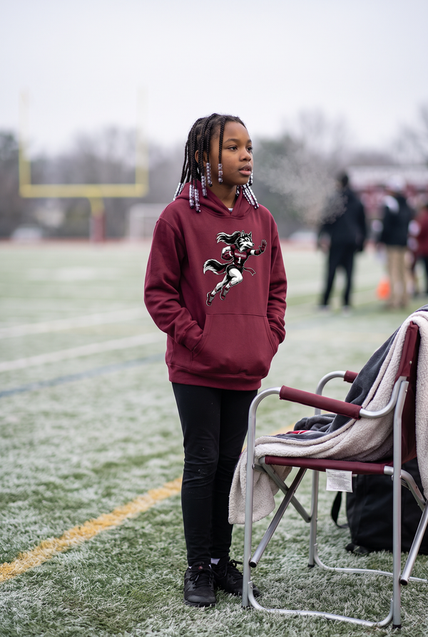 Woodcreek Girls Flag Football Stiff Arm Youth Hoodie in Maroon, worn on a cold-morning sideline